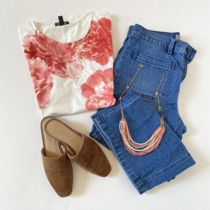 A flatlay view of a vintage J.Crew flower tee shirt styled with jeans, a pink necklace and flats