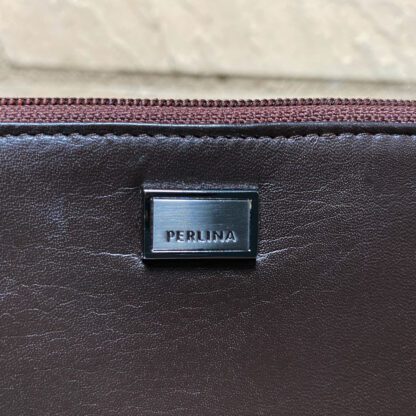 Close-up view of the front of a vintage Perlina wallet, showing the leather and the metal logo.