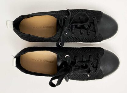 Top view of a pair of Banana Republic black flyknit low-top sneakers for women, showing the black uppers, white sole, leather insole with Banana Republic brnad name and black tie laces.