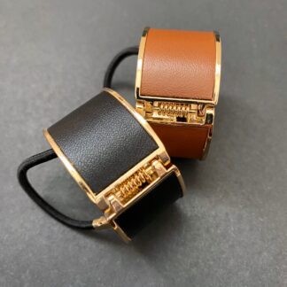 two leather and metal ponytail covers with elastic, shown in black and tan leeather