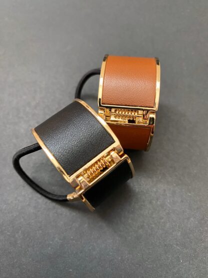 two leather and metal ponytail covers with elastic, shown in black and tan leeather